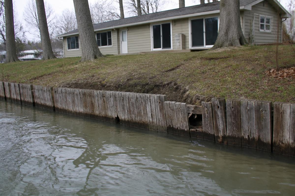 Aging timber seawall at a lake house with gaps between boards and soil washed out behind the wall